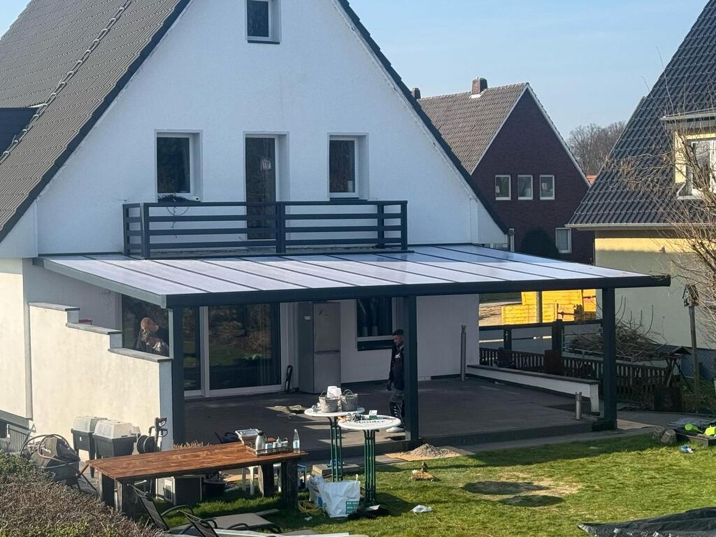 Zwei Personen arbeiten an einem weißen Haus mit Terrasse und dunklem Dach in einem Wohngebiet.