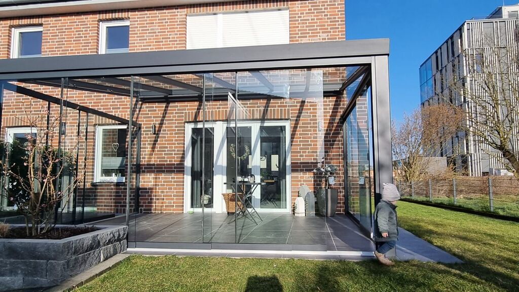 Ein Kind in Winterkleidung schaut auf einen verglasten Wintergarten eines modernen Backsteinhauses.