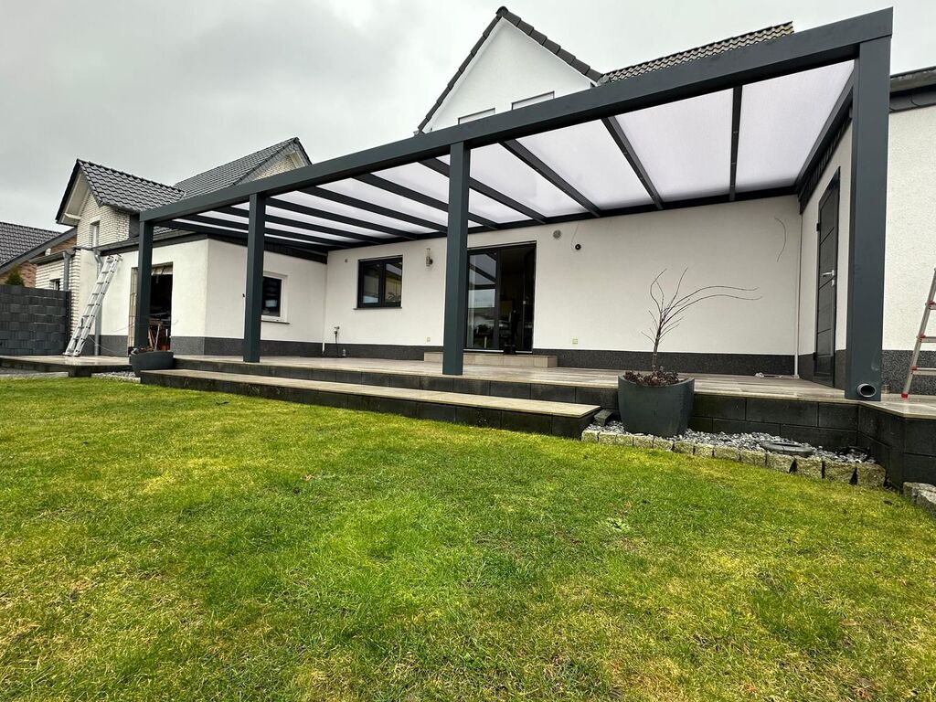 Ein modernes Haus mit Terrasse und Rasen; grauer Himmel im Hintergrund.