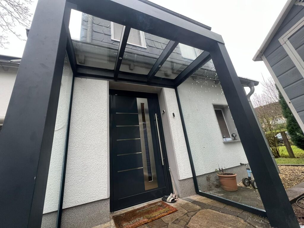 Moderne Haustür mit Glasüberdachung und weißen Wänden; schlichte Architektur; graue Akzente.