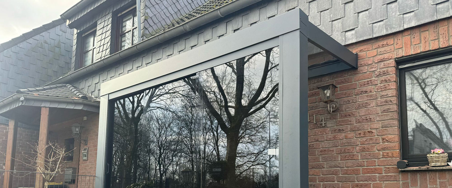 Altes Backsteinhaus mit modernem, grauem Wintergartenanbau und reflektierenden Fenstern.