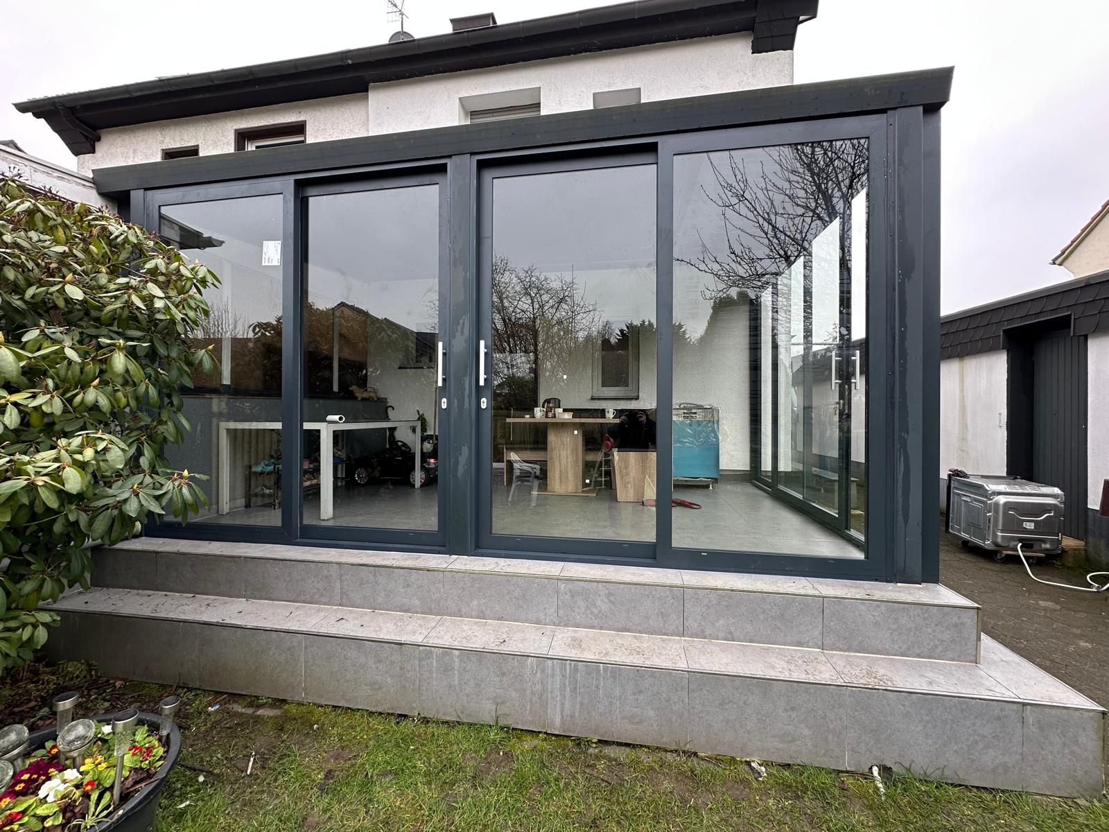 Modernes Wohnzimmer mit großen Glasfenstern, grau und weiß, Gartensicht, schlicht.