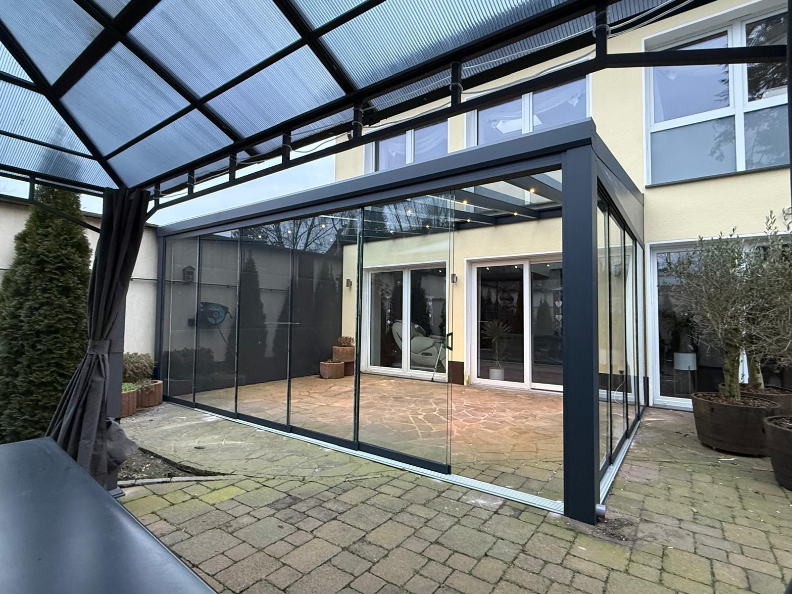 Modernes Wintergarten-Design mit Glaswänden, überdachter Außenbereich, graue Struktur.