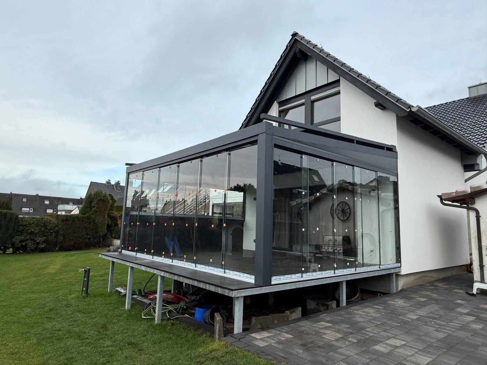 Wintergarten aus Glas an einem Einfamilienhaus mit schwarzem Dach und gepflegtem Rasen.