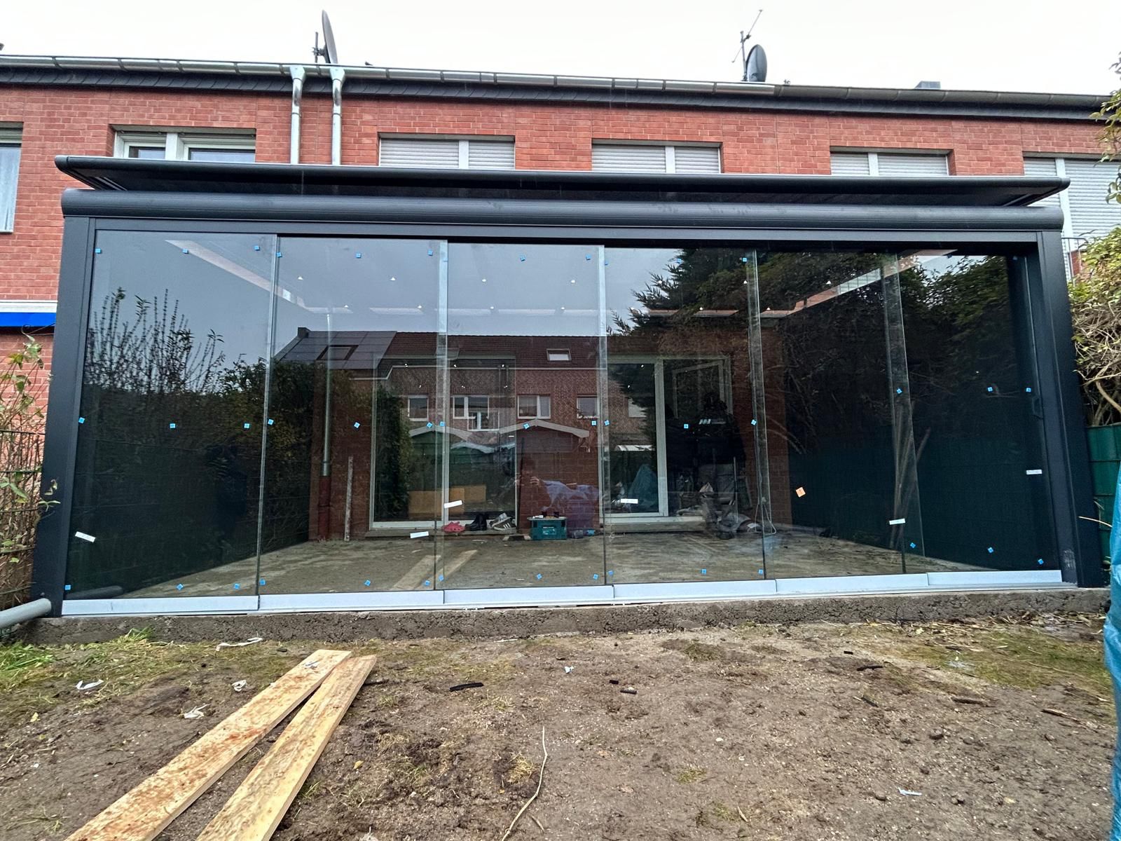 Hausrückseite mit Glasveranda, moderner Stil, rote Ziegel, Glasschiebetüren, trübes Wetter.