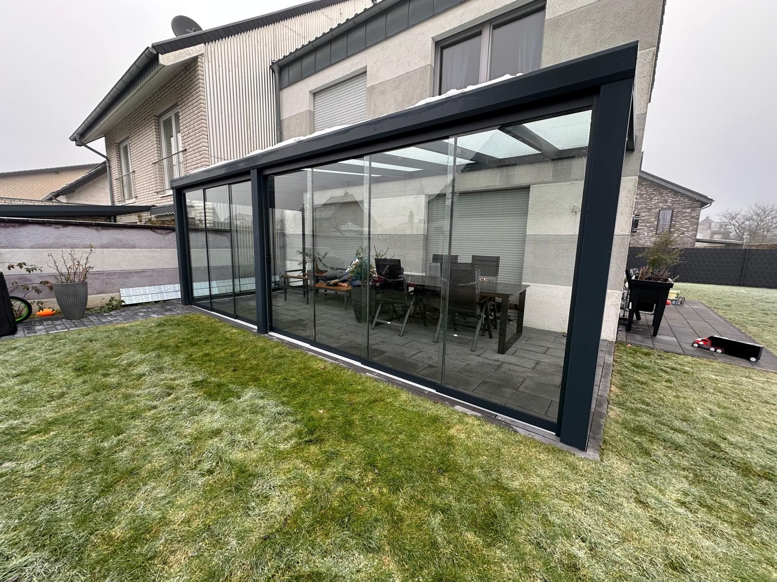 Ein modernes Haus mit einem Wintergarten aus Glas und einer gepflegten Rasenfläche im Vordergrund.